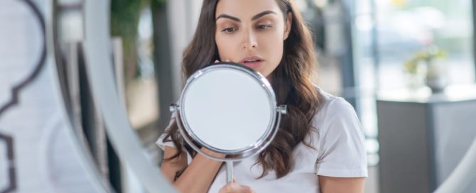 Woman examining overdoing skincare symptoms in mirror