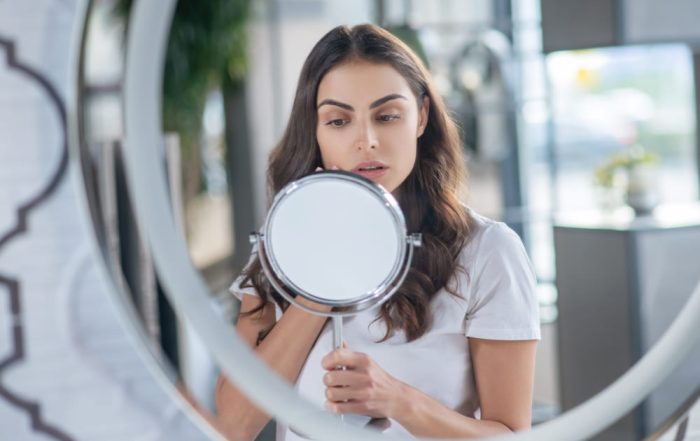 Woman examining overdoing skincare symptoms in mirror